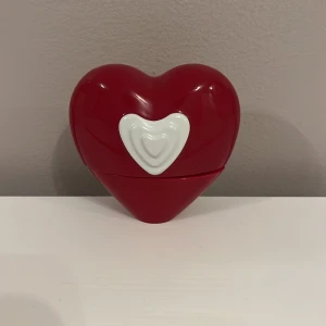 Hjärtaformad parfymflaska från ESCADA - Charmig parfymflaska i form av ett rött hjärta med en vit detalj framtill. Flaskan har en gyllene spraydel och är perfekt för den som älskar unika och romantiska designinslag i sin parfymsamling.