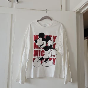 Vit långärmad pyjamas tröja med Mickey Mouse från H&M - Säljer en vit långärmad pyjamas tröja från H&M med ett stort tryck av Mickey Mouse i svart och rött. Perfekt för Disney-fans som vill ha en bekväm och stilren look. Tröjan är tillverkad i 100% bomull. Är i mycket bra skick, bara legat i lådan. 