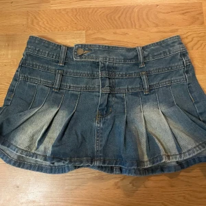 Mini jeanskjol  - Aldrig använd nygg kort jeanskjol med veck och bälteshällor. Kjolen har en knapp och dragkedja framtill. Original pris 300kr
