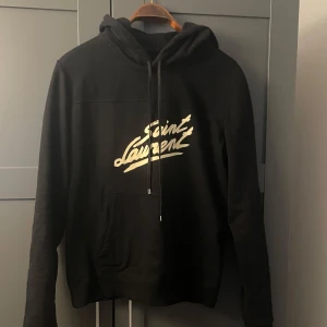 Svart Saint Laurent luvtröja - Snygg hoodie från Saint Laurent. Lappen där det står M sitter längre ner i hoodien på insidan. Bra skick inga defekter. Finns ej en lapp i nacken (vet ej om den är borta eller om det är meningen att vara så) Har inga äktighetsbevis så kan inte garantera med 100% säkerhet att den är äkta men den borde vara det