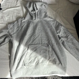 Grå hoodie från Grunt - Säljer en stilren grå hoodie från Grunt i storlek XL. Den har en klassisk känguruficka och en bekväm huva. Perfekt för en avslappnad look.