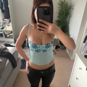 Ljusblå linnetopp med blommönster - Säljer en söt ljusblå linnetopp med smala axelband och blommigt mönster i mörkblått. Toppen är croppad och har en feminin design som passar perfekt för varma dagar.