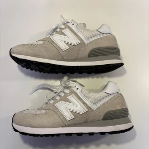 New Balance 574 - Snygga och bekväma beigea/gråa sneakers från New Balance med vit snörning och svart sula. Skorna är knappt använda. Modellen är Newbalance Classic 574, nypris cirka 1300kr