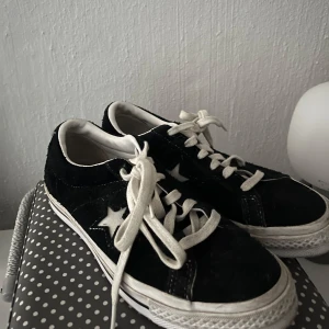 Svarta sneakers från Converse - Snygga svarta sneakers från Converse med vita stjärndetaljer på sidan. Skorna har en klassisk design med snörning och en bekväm sula. Perfekta för en avslappnad stil.