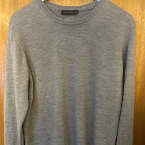 Grå tröja från Oscar Jacobson - Säljer en stilren grå tröja från Oscar Jacobson. Tröjan har en klassisk rund hals och är tillverkad i ett mjukt material. Perfekt för en elegant och avslappnad look.