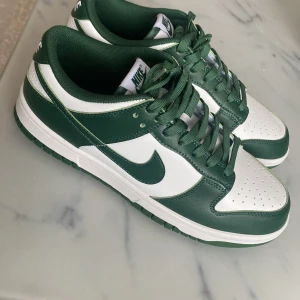 Nike Dunk i grönt och vitt - Snygga Nike Dunk sneakers i en fräsch grön och vit färgkombination. Skorna har klassisk snörning och en rund tå. Perfekta för dig som vill ha en stilren look med en sportig touch. Köp dem nu och uppgradera din sneakerkollektion! 💚har tyvärr inte boxen kvar. Skorna ligger på ca 1,7 ord pris 