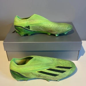 Adidas x speedportal + AG elit - Snygga gröna fotbollsskor från Adidas med en strömlinjeformad design och svarta detaljer. Skorna har en mönstrad sula för optimalt grepp på planen. Perfekta för den som vill sticka ut på fotbollsplanen.      