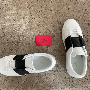 Valentino Open sneakers i vitt och svart - Snygga Valentino Open sneakers i vitt med svart detalj. Använda av mig ett antal gånger men är lite stora. Har fixat till de så gott jag kan. Storlek 46!