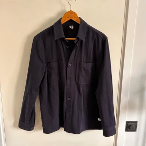 Svart långärmad skjorta - Snygg svart långärmad skjorta med knappar framtill och två bröstfickor. Storlek 50 men klassas som M. Knappt använd och bra för vår sommar och höst. 