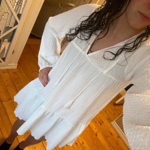 Vit klänning från Gina Tricot - Säljer en oanvänd (då den är för kort på mig som är 172) vit klänning från Gina Tricot med lång ärm och volangdetaljer. Klänningen har en lös passform och är perfekt för sommaren. Den har en v-ringad hals och knytband fram.