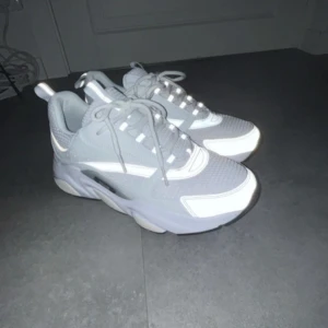 Vita sneakers b22 - Snygga vita sneakers från ett känd märke  med grå detaljer och snörning. Skorna har en chunky sula och är tillverkade i syntetmaterial med meshdetaljer för en modern look.
