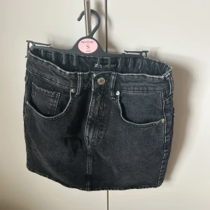 Svart jeanskjol från Zara - Snygg svart jeanskjol från Zara i storlek XS. Kjolen har en klassisk femficksdesign med knapp och dragkedja framtill. Perfekt för en cool och avslappnad stil.