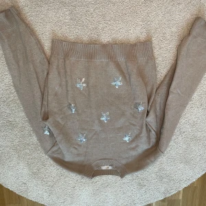 Beige tröja med stjärnor från Gina Tricot - Säljer en beige tröja från Gina Tricot med glittriga stjärnor på framsidan. Tröjan har långa ärmar och ribbade kanter vid hals, ärmslut och nederkant. Perfekt för en mysig dag! ✨