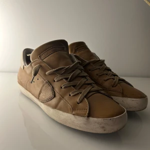 Bruna sneakers från Philippe Model - Snygga bruna sneakers från Philippe Model i skinn med klassisk snörning. Skorna har en rund tå och en vit sula som ger en stilren look. Perfekta för en avslappnad stil. Skorna är i använt skick men har mycket kvar att ge😇De har en del deftekter på lädret och sulan. Kontakta mig om ni har funderingar!