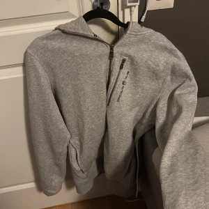 Grå hoodie från Sail Racing - Säljer en stilren grå hoodie från Sail Racing med dragkedja och logotyp på bröstet. Tröjan har en bekväm passform och är perfekt för kyligare dagar. Den har långa ärmar och en praktisk huva.