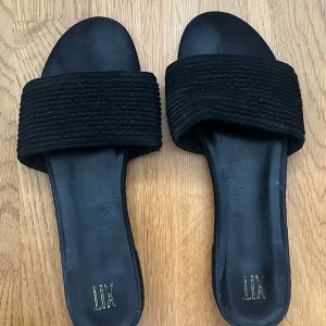 Svarta sandaler från LIX - Snygga svarta sandaler från LIX med en bred ribbad rem över foten. Perfekta för en avslappnad stil under varma dagar. Sandalerna har en öppen tå-design och en platt sula för komfort.