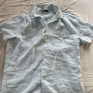 Ljusblå linneskjorta från J.Lindeberg - Fin linneskjorta från J.Lindberg som är perfekt för sommaren. Jag köpte denna förra sommaren men den passade tyvärr inte mig. Den är använd 1 gång och i mycket bra skick.