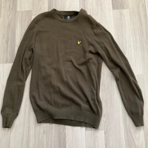Grön stickad tröja från Lyle & Scott - Snygg grön stickad tröja från Lyle & Scott i storlek s. Klassisk rund halsringning och långärmad modell med den ikoniska gula örnloggan broderad på bröstet. Perfekt för lager-på-lager och chill höst- eller vinterstil.