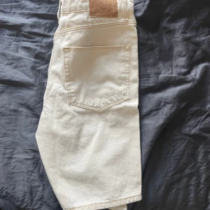 Vita jeansshorts från ASOS DESIGN - Snygga vita jeansshorts från ASOS DESIGN med klassisk femficksmodell och gylf med knapp. De är raka i modellen och har en midwaist-passform. Perfekta för sommardagar och lätta att matcha med allt.