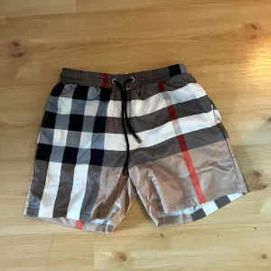 Rutig badshorts från Burberry - Snygga shorts till sommaren. Säljer dom för att dom var för små för mig när jag köpte dom. Storlek M men passar S. Byxorna är inte äkta!!! Hör av er vid minsta fundering, Pris kan diskuteras! 