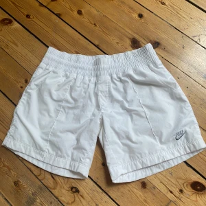 Vita Nike shorts med resårmidja. Eftersom den är strethig i midjan så är den s-xs  - Fräscha vita lågmidjade shorts från Nike med elastisk midja och sidofickor. Klassisk sportig look med diskret Nike-logga broderad framtill. Lätta och sköna, perfekta för sommaren eller träning. Tillverkade i mjukt material som andas.