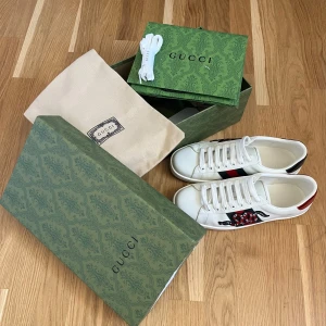 Gucci ace snake - Ett par snygga gucci ace snakes i mint condition. Skorna har vit snörning, rund tå och platt sula. Baksidan har röda och gröna detaljer. Perfekta för dig som vill sticka ut med lyxig streetstyle. Smått använda men som nya, inga skador varken utanför eller innanför skorna.