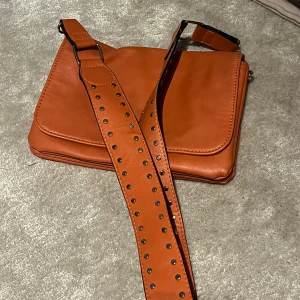 Orange axelväska - Orange crossbodyväska med snyggt axelband. Har två pack på insidan och ändå rymlig trots sin storlek. 