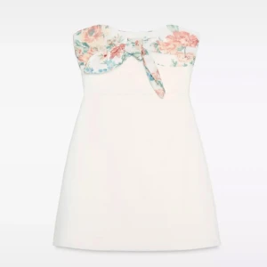 Söt klänning från zara🥹🥹 - Supersöt vit klänning från zara med blommönster på bröstet!! På bilderna har jag vikt in rosetten så man inte ser den men den är lika fin med☺️☺️Änvänd en gång!!