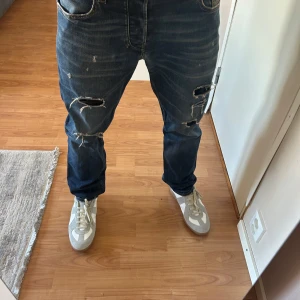Diesel jeans  - Säljer ett par blå jeans från Diesel med coola slitningar och hål på båda benen. Jeansen har klassisk femficksdesign, normal passform och är gjorda i robust denim. Perfekta för dig som gillar en avslappnad och edgy stil. Dem har ett litet hål som jag har sytt ihop. Därför lägger jag ut det så billigt 