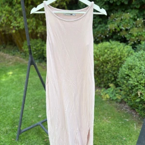 Ljusbeige långklänning från 157 - Enkel och stilren långklänning i ljusrosa från 157. Ärmlös modell med rund halsringning och rak passform. Perfekt för varma dagar och enkel att styla med accessoarer. Mjuk och lätt i materialet, vilket gör den superbekväm.