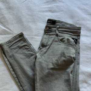 Replay Anbass grå slim jeans - Snygga grå jeans från Replay, modell Anbass med slim fit. Klassisk femficksdesign, diskret Replay-logga vid fickan och bekvämt stretchigt jeanstyg. Perfekta för dig som gillar en smalare passform och stilren look.