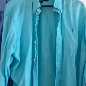 Turkos linneskjorta Ralph Lauren XL - Snygg turkos skjorta från Ralph Lauren i linne med slim fit-passform. Klassisk krage, knäppning framtill och broderad logga på bröstet. Perfekt för dig som gillar en fräsch och luftig stil under varmare dagar.