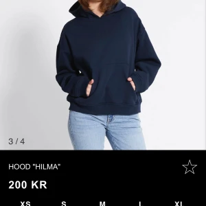 Mörkblå hoodie Hilma - Säljer en mörkblå hoodie från Hilma med klassisk huva och känguruficka framtill. Tröjan har en loose passform och är tillverkad i mjuk bomullsmix, perfekt för chill dagar. Långa ärmar och ribbade muddar ger en skön och avslappnad look.