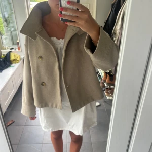 Beige ulljacka med stora knappar - Snygg beige jacka i ull med bred krage och stora, stilrena knappar framtill. Jackan har en boxig, lite oversized passform och långa ärmar. Perfekt för dig som gillar minimalistisk och clean stil.