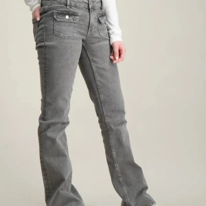 Grå bootcut jeans med fickdetaljer - Snygga grå jeans med bootcut passform och coola fickor framtill med lock och knapp. Jeansen är från Gina Young i storlek 164 vilket motsvarar xs-s de finns knapp på insidan i jeansen vilket gör att man kan justera vid midjan. Nypris 350