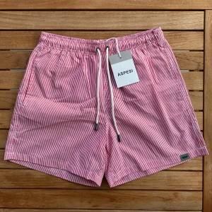 Aspesi Badbyxor Randiga M - Snygga röda och vita badshorts från Aspesi med smala ränder och elastisk midja. Helt nya med tags, inga defekter förekommer. Perfekta för stranden eller poolen. Ordinarie nypris ca 2000:-