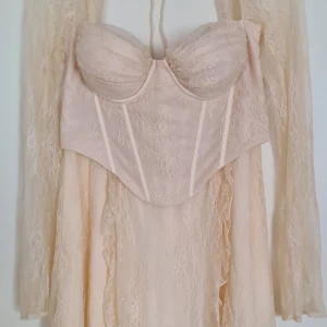 Champagnefärgad spetsklänning Oh Polly - Magisk kort klänning från Oh Polly i champagnefärgad spets. Klänningen har långärmade ärmar, markerad byst med corsettdetaljer. Perfekt för dig som vill sticka ut med romantisk och feminin stil. Klänningen är aldrig använd och har taggarna kvar! Sista bilden från Oh Polly's hemsida.