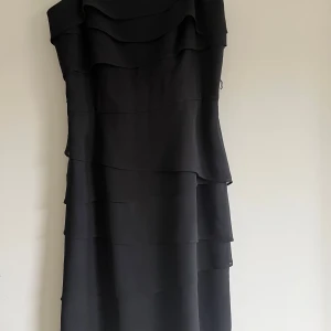 Svart långklänning med volanger - Snygg svart långklänning med flera lager volanger som ger en cool och elegant look. Axelbandslös design som passar perfekt när du vill sticka ut. Klänningen har en flowy känsla och är riktigt stilren.