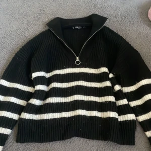 Svartvit randig stickad tröja FB Sister - Säljer en svart stickad tröja från FB Sister med vita horisontella ränder. Tröjan har en ribbad struktur, lång ärm och en snygg half zip-dragkedja med rund ring. Perfekt för dig som gillar en chill och trendig look.
