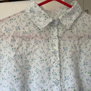 Vit blommig skjorta med trekvartsärm - Söt vit skjorta med små blå och gröna blommor, klassisk krage och knäppning framtill. Skjortan har trekvartsärmar och är gjord i ett lätt bomullstyg, perfekt för varmare dagar. Passar dig som gillar romantiska och fräscha vibes. Oversized 