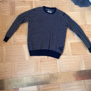 Randig stickad tröja från Barbour - Mörkblå och vit randig stickad tröja från Barbour i storlek S. Tröjan har lång ärm, ribbade muddar och en snygg detalj med knapp nertill. Perfekt för dig som gillar klassisk stil med en twist. Pris kan diskuteras vid snabb affär.