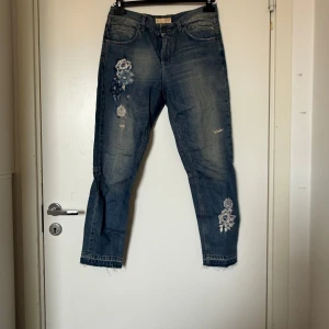 Odd Molly jeans med broderade blommor - Snygga blå jeans från Odd Molly med broderade blommor i vitt och blått på benet och vid benslut. Jeansen har croppad längd, råa kanter nertill och en relaxed fit. Perfekta för dig som vill ha något unikt och trendigt i garderoben. Från märket Odd Molly i storlek 0 som ungefär motsvarar en Storlek XS, men dessa är mer en S/M. Fint skick, men de är fortfarande mer använda och kan vara något missfärgade. Se bilder. 