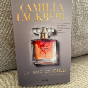 En bur av guld. Inbunden bok  - En snygg och spännande bok med ett lockande omslag som visar en parfymflaska med ordet 'Revenge'. Perfekt för dig som gillar dramatiska berättelser och starka känslor. Passar unga vuxna som vill ha något fängslande att läsa.