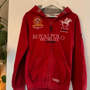 Röd hoodiejacka Geographical Norway M - Röd hoodiejacka från Geographical Norway med broderade detaljer, dragkedja och huva. Jackan har stora vita och svarta brodyrer framtill och på ärmen, samt fickor och ribbade muddar. Perfekt för dig som gillar sportig och avslappnad stil. Den är använd men i bra skick. Finns någon tråd och lite nopprig, men hela muddar/dragkedja och överlag bra skick. 
