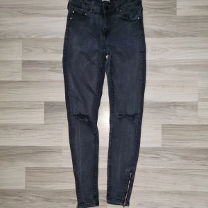 Svarta skinny jeans med dragkedja - Snygga svarts skinny jeans från 157 med slitna knän och dragkedjor vid bensluten. Jeansen har klassisk femficksdesign och smal passform som sitter tight hela vägen ner. Perfekta för dig som gillar en edgy och trendig look.