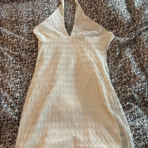 Vit halterneck klänning från H&M  - Supersöt vit kortklänning från H&M med halterneck och v-ringning. Klänningen har ett vågigt spetsmönster över hela och är fodrad med satinliknande tyg. Storlek S. Den är helt oanvänd med prislapp på. Nypris 149kr.