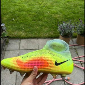 Nike fotbollsskor 43 - Snygga fotbollsskor från Nike i neonfärger med svart swoosh. Skorna har en hög strumpkrage och är gjorda i syntetmaterial med snörning. Färgerna går i gult, orange och rött med cool gradient-effekt. Perfekta för dig som vill sticka ut på planen.