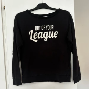 Svart tröja med tryck från H&M - Svart långärmad tröja från H&M med vit text 'Out of your League' på bröstet. Tröjan har rund halsringning och långa ärmar. Storlek S, men passar även om man har storlek M. Aldrig använd. 