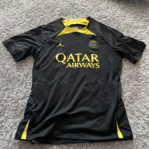 PSG x Jordan svart/gul fotbollströja M - PSG fotbollströja från Jordan i svart med gula detaljer och loggor. Qatar Airways tryck på bröstet, klassisk rund hals och korta ärmar. Slim fit-modell i lätt och ventilerande material, perfekt för match eller träning. Knappt använd.