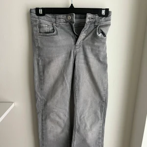 Grå jeansbyxor i rak modell - Snygga grå jeansbyxor i rak passform med klassiska fem fickor och dragkedjegylf. Jeansen har en ljusgrå tvätt och är tillverkade i mjukt denimtyg. Perfekta för en chill och stilren look.